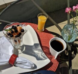 outdoor table setting with fruit parfait, orange juice and a cup of coffee